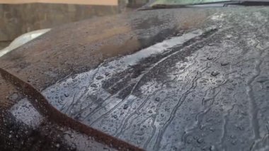 Siyah arabanın kaputuna yağmur yağıyor. Siyah bir arabanın kaputundan güzel bir şekilde damlıyor..
