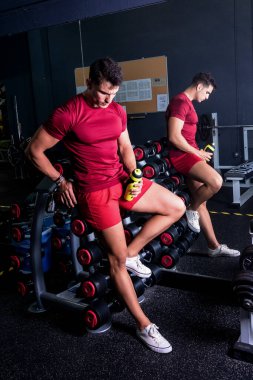 Mola zamanı. Spor kıyafetli genç adam spor salonunda otururken elinde bir şişe su tutuyor..