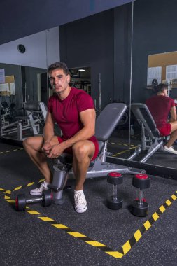 Mola zamanı. Spor kıyafetli genç adam spor salonunda oturuyor..