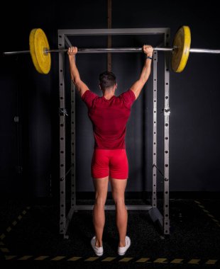 Genç vücut geliştirici spor salonunda omzunu çalıştırıyor..