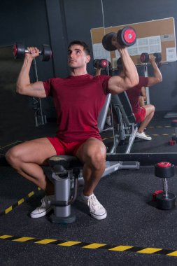 Genç vücut geliştirici spor salonunda omzunu çalıştırıyor..