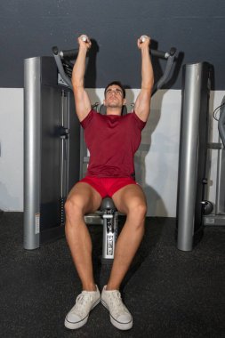 Genç vücut geliştirici, basın makinesinde omzunu çalıştırıyor..