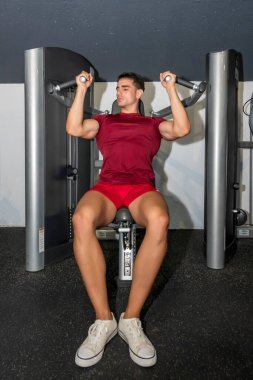 Genç vücut geliştirici, basın makinesinde omzunu çalıştırıyor..