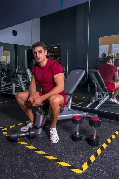 Mola zamanı. Spor kıyafetli genç adam spor salonunda oturuyor..
