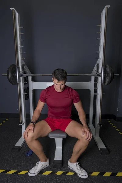 Mola zamanı. Spor kıyafetli genç adam spor salonunda oturuyor..