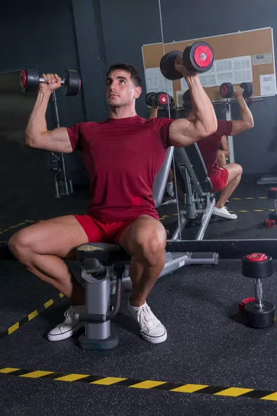 Genç vücut geliştirici spor salonunda omzunu çalıştırıyor..