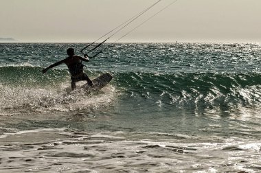 A young professional kitesurfer rides a board along the surface of the sea at sunset