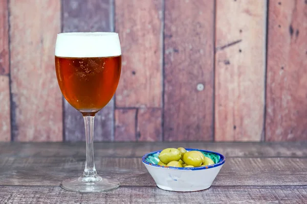Glass of fresh beer with a cap of green olives. Wood background.