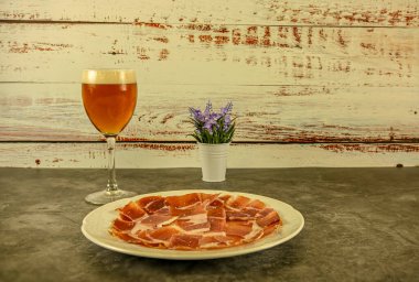 Bir tabak Serrano jambonu, taze kesilmiş ve bir bardak birayla servis edilmiş.