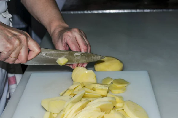 Professional chef cuts knife potatoes on white board.