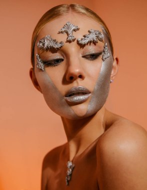 Sarışın bir kadın gibi güzel bir heykelin güzel stüdyo portresi. Mükemmel bir cilde, makyaja ve yüz sanatına sahip. Turuncu duvar arkasında çıplak poz veriyor.. 