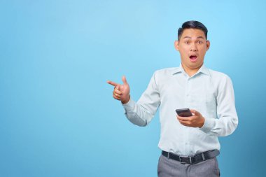 Şok olmuş genç yakışıklı işadamı akıllı telefonu tutuyor ve fotokopi alanını işaret ediyor.