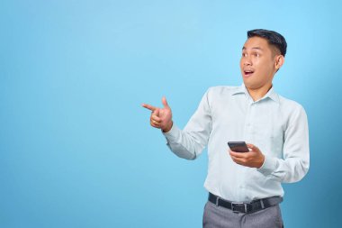 Şok olmuş genç yakışıklı işadamı akıllı telefonu tutuyor ve fotokopi alanını işaret ediyor.