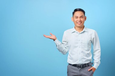 Gülümseyen genç ve yakışıklı iş adamı mavi arka planda avuçlarında kopya alanı gösteriyor