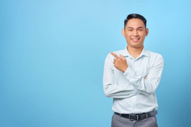 Gülümseyen yakışıklı iş adamı mavi arka plandaki kopya alanını işaret ediyor.