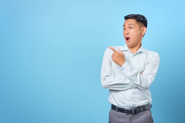 Şok olmuş genç yakışıklı işadamı mavi arka plandaki fotokopi alanını işaret ediyor