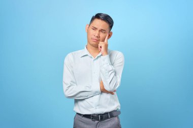 Dalgın genç ve yakışıklı işadamı mavi arka plandaki soruları düşünüyor.