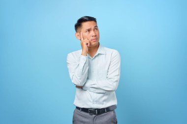 Dalgın genç ve yakışıklı işadamı mavi arka plandaki soruları düşünüyor.