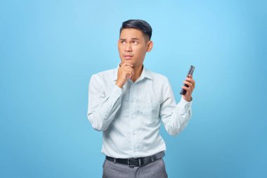 Ciddi, genç, yakışıklı bir iş adamı elinde akıllı bir telefon tutup düşünceli bir ifadeyle yukarı bakıyor.