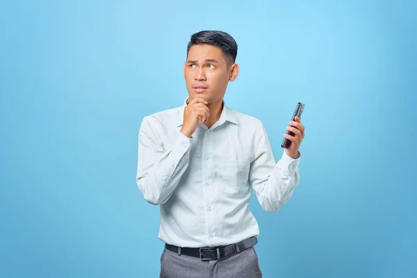 Ciddi, genç, yakışıklı bir iş adamı elinde akıllı bir telefon tutup düşünceli bir ifadeyle yukarı bakıyor.