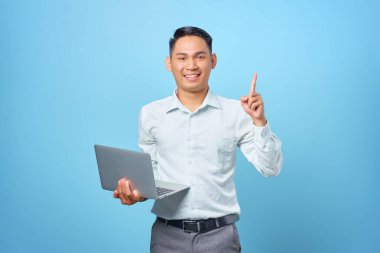 Mavi arka planda dizüstü bilgisayar tutarken yaratıcı bir fikri olan genç ve mutlu bir iş adamı.