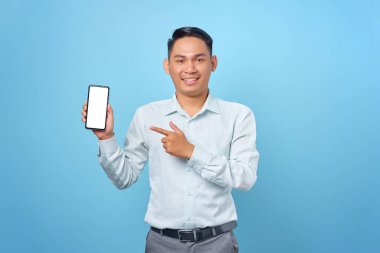 Gülümseyen genç yakışıklı iş adamı mavi arka plandaki boş ekranı işaret ediyor.