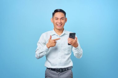 Gülümseyen genç yakışıklı işadamının portresi mavi arka plandaki akıllı telefonu işaret ediyor.