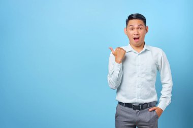 Şaşırmış genç yakışıklı iş adamı mavi arka plandaki fotokopi alanını işaret ediyor