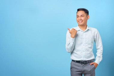 Gülümseyen yakışıklı iş adamı mavi arka plandaki kopya alanını işaret ediyor.