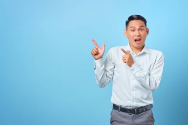 Şok olmuş genç yakışıklı işadamı mavi arka plandaki fotokopi alanını işaret ediyor