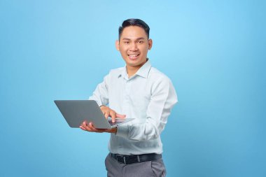 Mavi arka planda elinde dizüstü bilgisayarla gülümseyen yakışıklı iş adamının portresi.