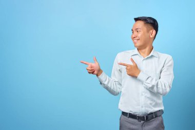 Gülümseyen yakışıklı iş adamı mavi arka plandaki kopya alanını işaret ediyor.