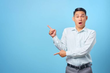 Şok olmuş genç yakışıklı işadamı mavi arka plandaki fotokopi alanını işaret ediyor