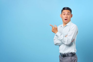 Şok olmuş genç yakışıklı işadamı mavi arka plandaki fotokopi alanını işaret ediyor