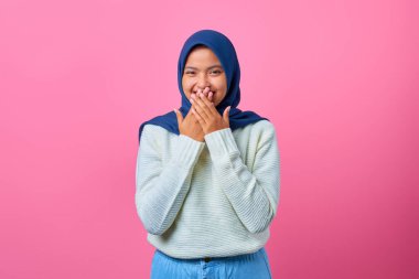 Gülümseyen Asyalı bir kadının portresi pembe arka planda elleri ile ağzını kapatıyor.