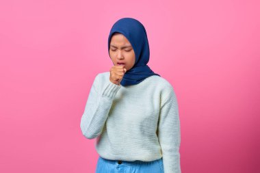 Güzel Asyalı kadın portresi kendini kötü hissediyor ve pembe arka planda öksürüyor.