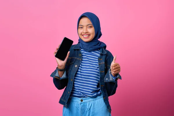 Gülümseyen Asyalı genç kadın portresi akıllı telefon boş ekranı gösteriyor ve baş parmak işareti yapıyor