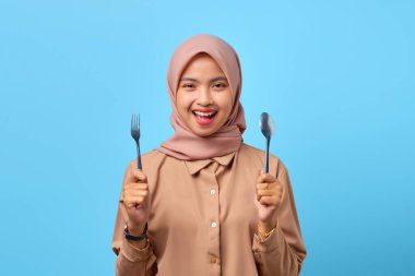Gülümseyen Asyalı genç kadının portresi çatal ve kaşıkla mavi arka planı kapatıyor.