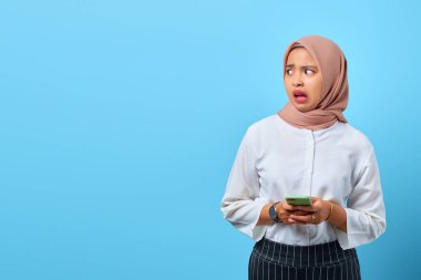 Şok olmuş Asyalı genç bir kadının portresi. Cep telefonu kullanıyor, ağzı açık ve yana bakıyor.