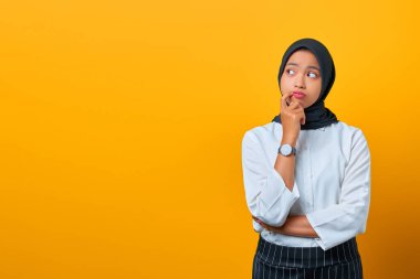 Düşünceli genç Asyalı kadın ciddi ciddi sarı arka plandaki bir soruyu düşünüyor gibi görünüyor.