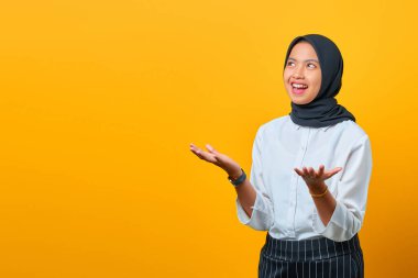 Çekici, gülen yüzlü, el kaldıran, sarı arka planda yaşayan Asyalı genç bir kadın.