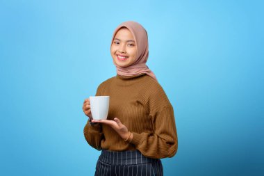 Asyalı güzel bir kadın elinde fincanla mavi arka planda çay içiyor.