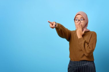 Şaşırmış güzel Asyalı kadının portresi mavi arka plandaki boşluğu işaret ediyor.