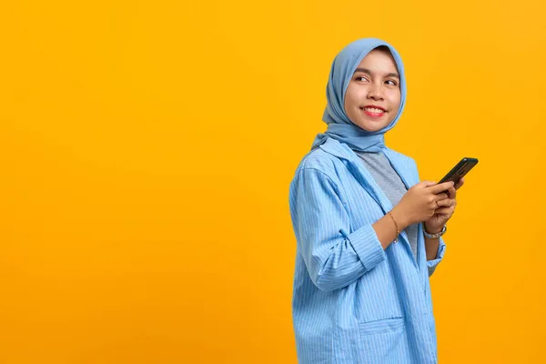 Fröhliche Junge Asiatin Nutzt Handy Und Blickt Zur Seite Auf — Stockfoto