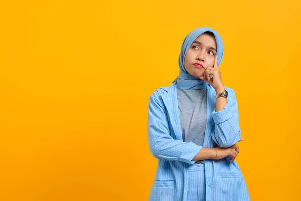 Pensive young Asian woman thinking about question with fingers on head over yellow background