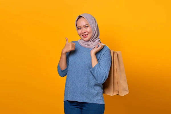 笑顔のアジアの女性の肖像ショッピングバッグを保持し 黄色の背景に親指を表示 — ストック写真