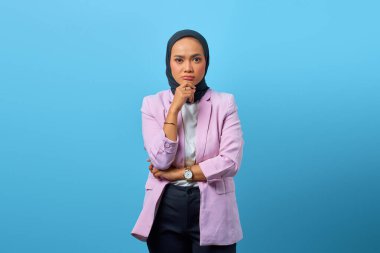 Güzel Asyalı kadın bir şey düşünür ve mavi arka planda çenesine dokunur.