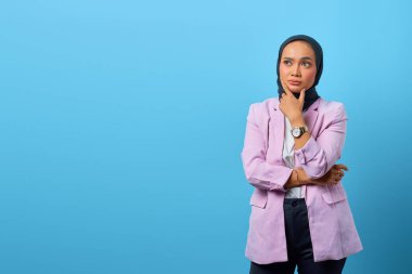 Güzel Asyalı kadın bir şey düşünür ve mavi arka planda çenesine dokunur.