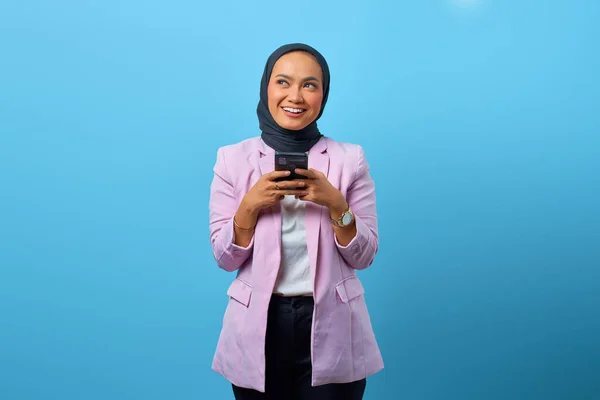 Neşeli Asyalı kadın cep telefonu tutuyor ve mavi arka plana bakıyor.