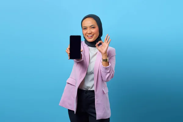 Neşeli Asyalı kadın akıllı telefon boş ekranı gösteriyor ve mavi arkaplanda işaret veriyor.